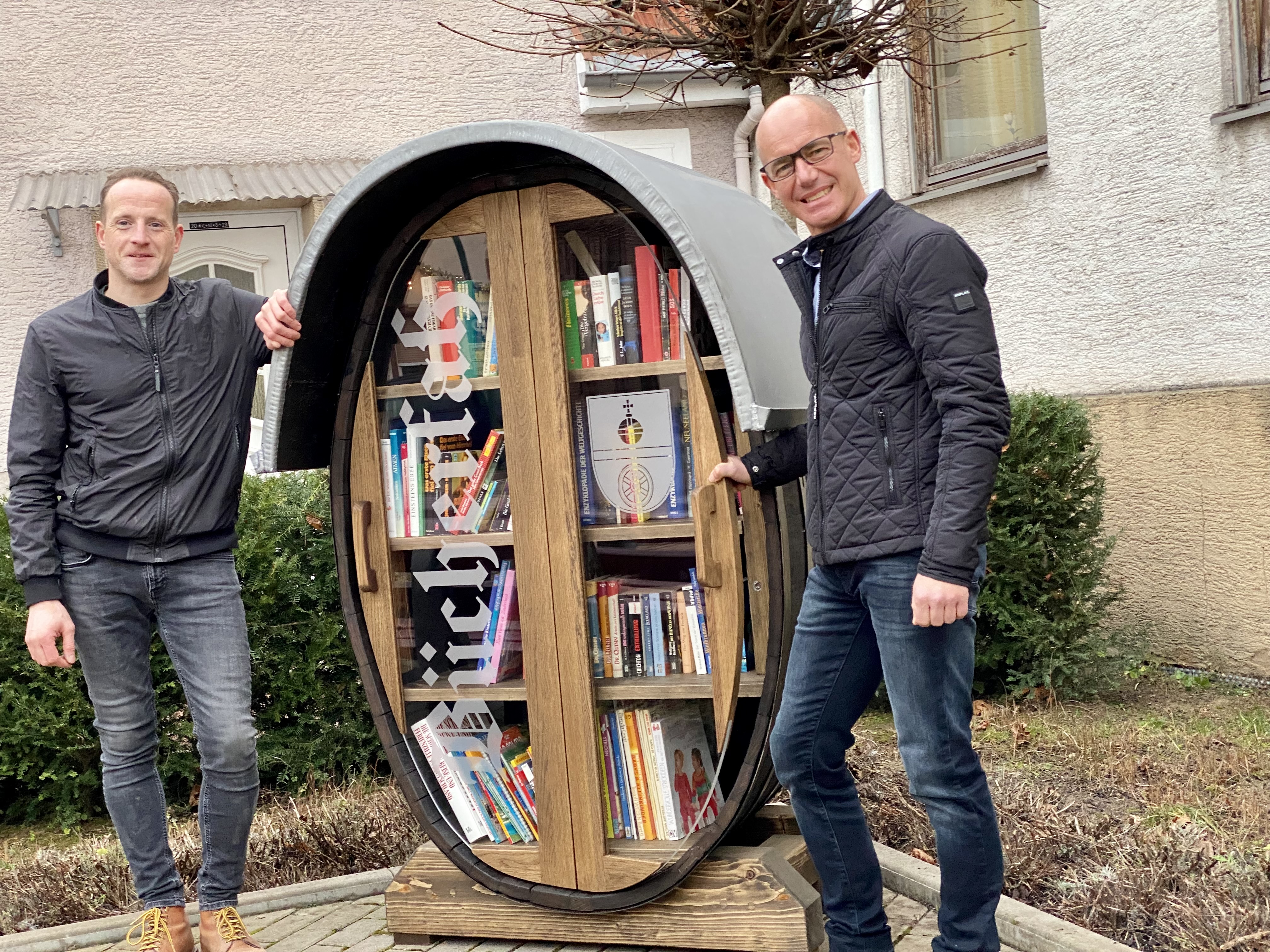 Dieses Bücherfass in Nackenheim als Miniatur-Bibliothek zeigt eine kreative Fusion von Literatur und Wein. Beigeordneter Jan Heckelsmüller (links) und Ortsbürgermeister René Adler (rechts) sind Gründungsmitglieder der Initiative „Wir für Nackenheim“, die das Projekt realisierte.